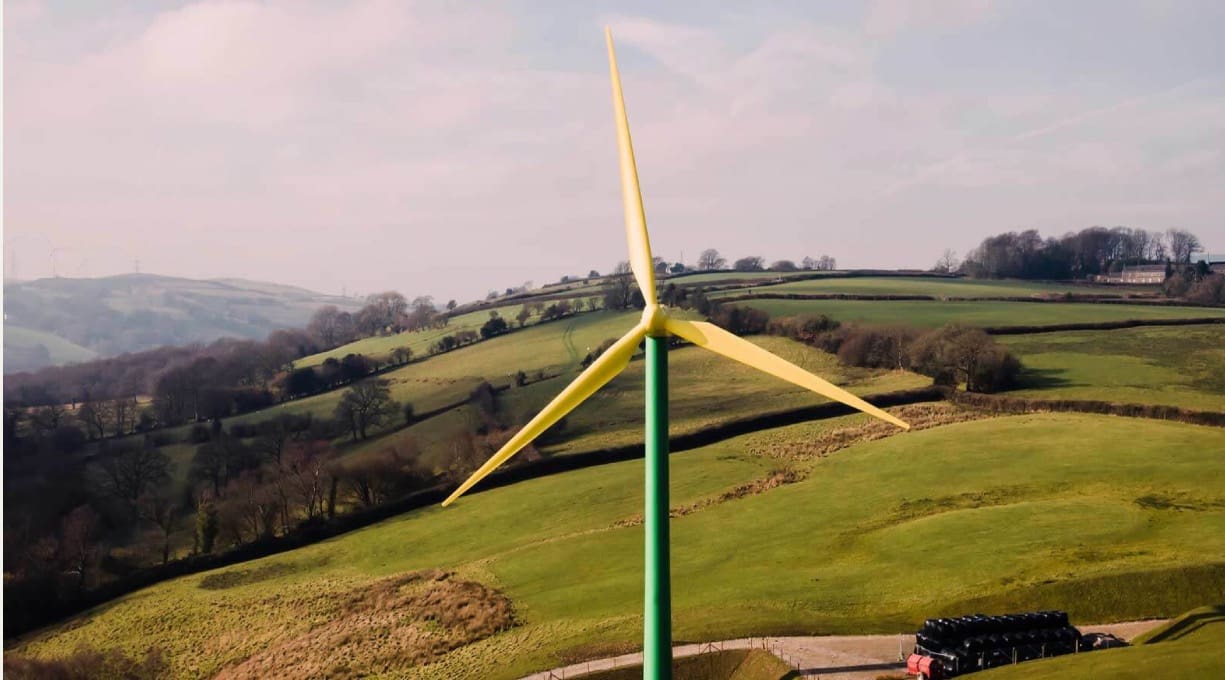 A windmill towers against a backdrop of rolling green fields