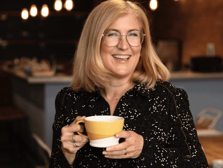 Tanith Sellicks, founder and director of Pure Table Top stands smiling with a mug of coffee