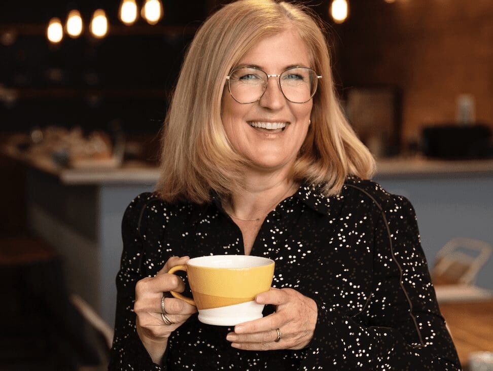 Tanith Sellicks, founder and director of Pure Table Top stands smiling with a mug of coffee