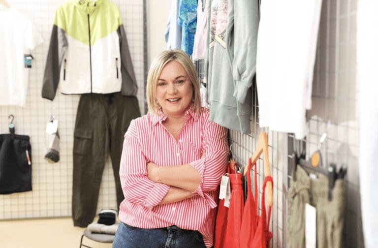 Lynne Walker, director of Primark Cares leans against a wall hung with Primark clothing