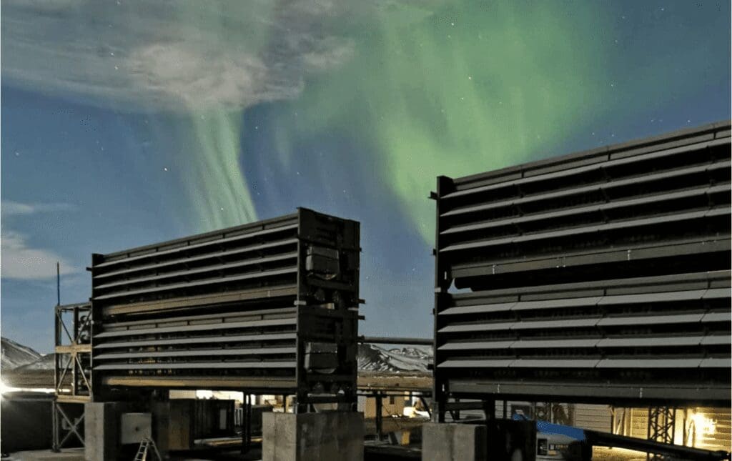 two buildings stand against dark sky with clouds of green light emanating from their roof tops.