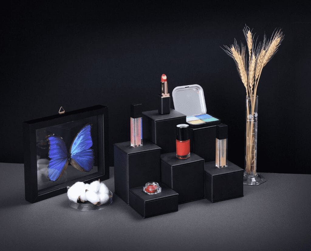 A collection of cosmetics products arranged on a black surface against a black background with moody lighting.