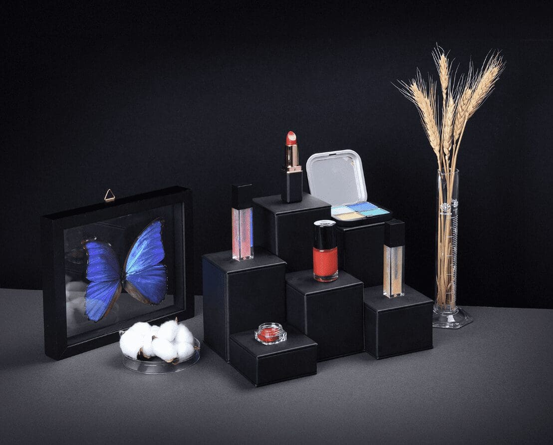 A collection of cosmetics products arranged on a black surface against a black background with moody lighting.