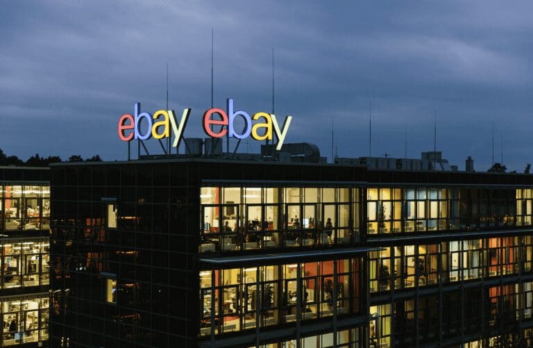 eBay office lit up against a moody dark sky with eBay logo in lights on top of the building.