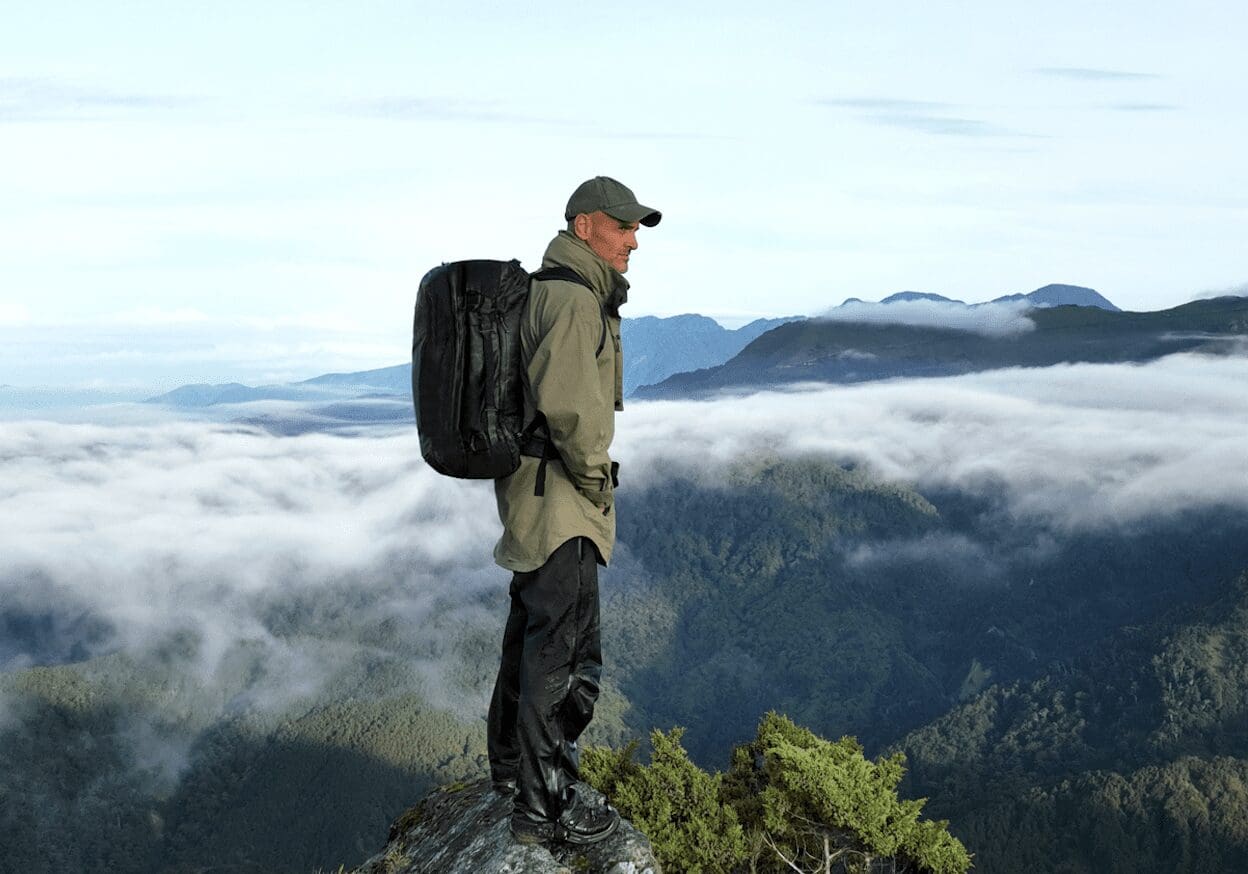 Ed Stafford stands atop a mounting wearing the Hybrid Duffle Pack and looking over the vista.