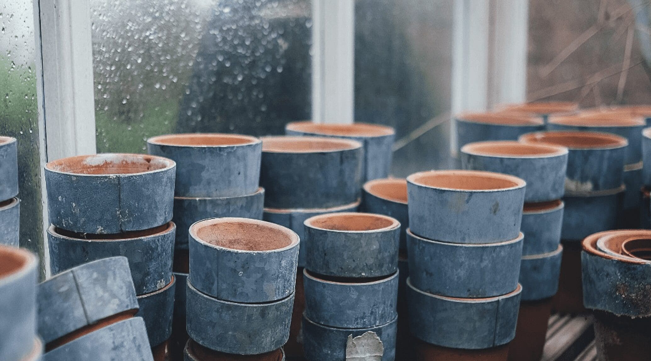 A closer of blue painted terracotta plant pots are stacked on a shelf by a window