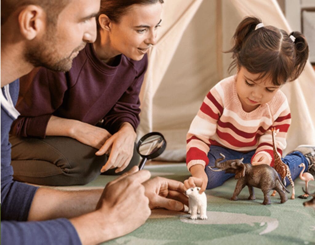 parents and a child are on the floor plying with Schleich figurines
