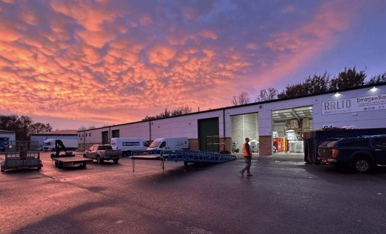 crimson sky as sun sets over a warehouse facility with man in high-vis jacket on the forecourt
