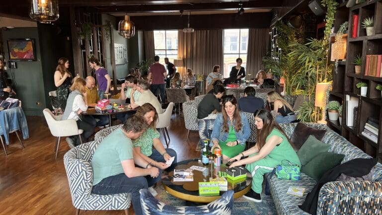Room full of people playing board games, looking happy, and chatting.