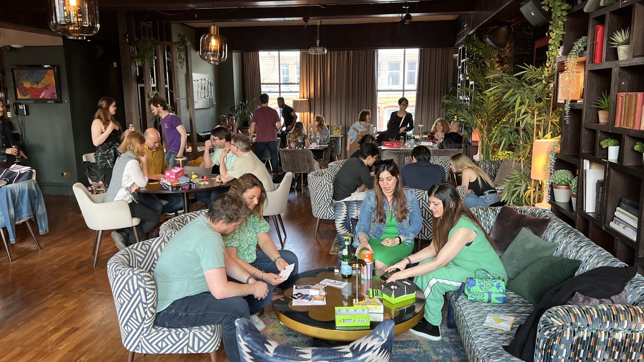 Room full of people playing board games, looking happy, and chatting.