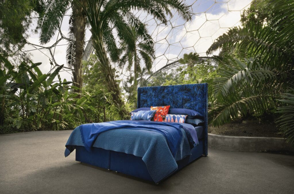 a blue bed with deep blue bedding is centred among tropical plants and trees found in the Eden Project biome