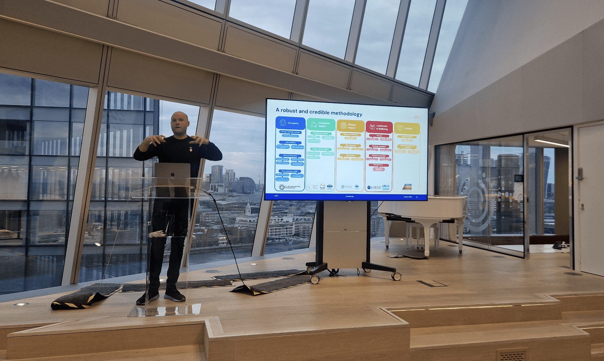 man stands on stage at a lecture and in front of a screen showcasing data