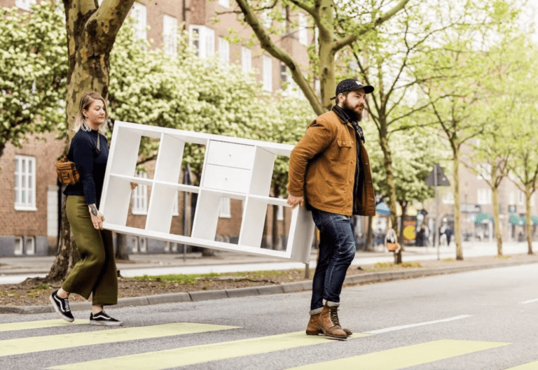 man and woman carry a cabinet across a road
