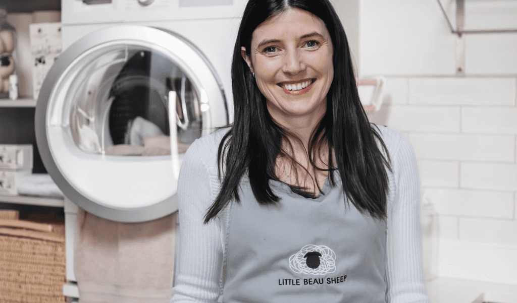 Little beau Sheep founder, Sarah Turner poses in front of tumble dryer in branded apron