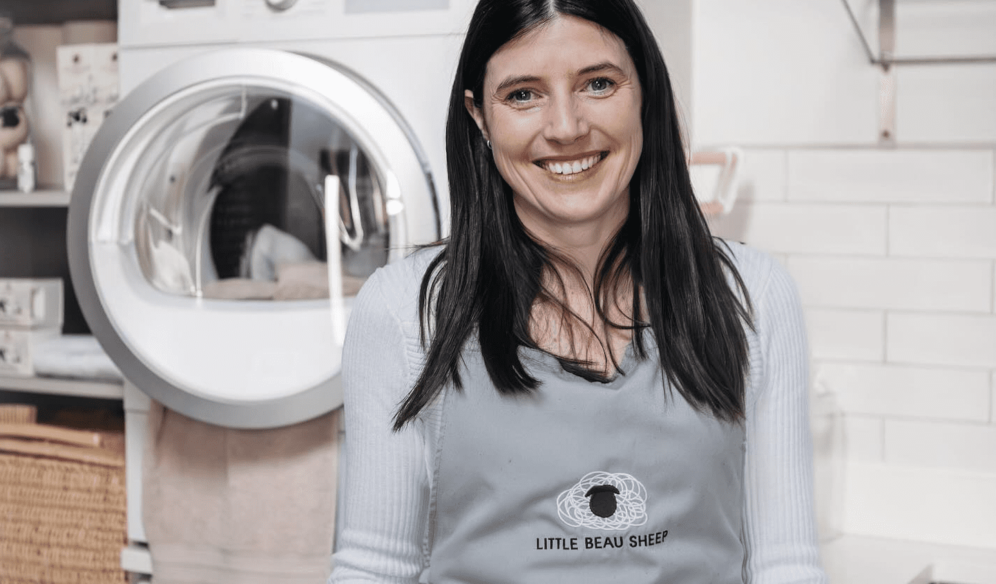 Little beau Sheep founder, Sarah Turner poses in front of tumble dryer in branded apron