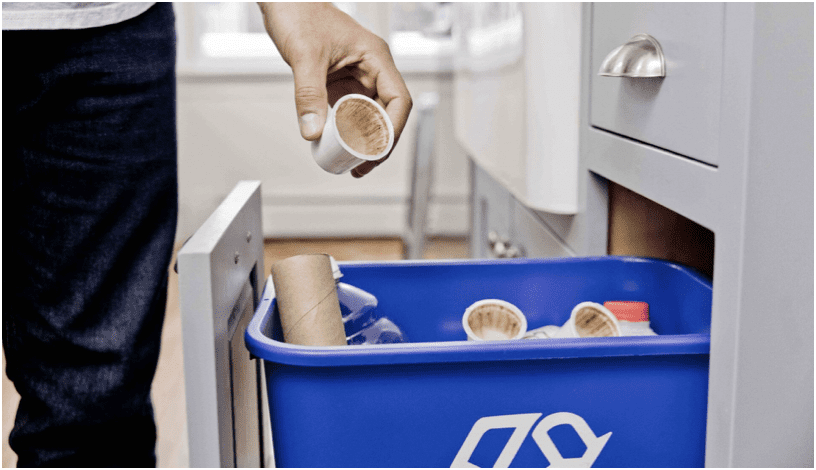 person dropping a recyclable coffee pod into a recycling bin at home