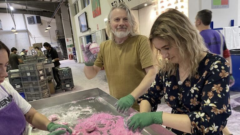 Three people stand round a table making pink bath bombs