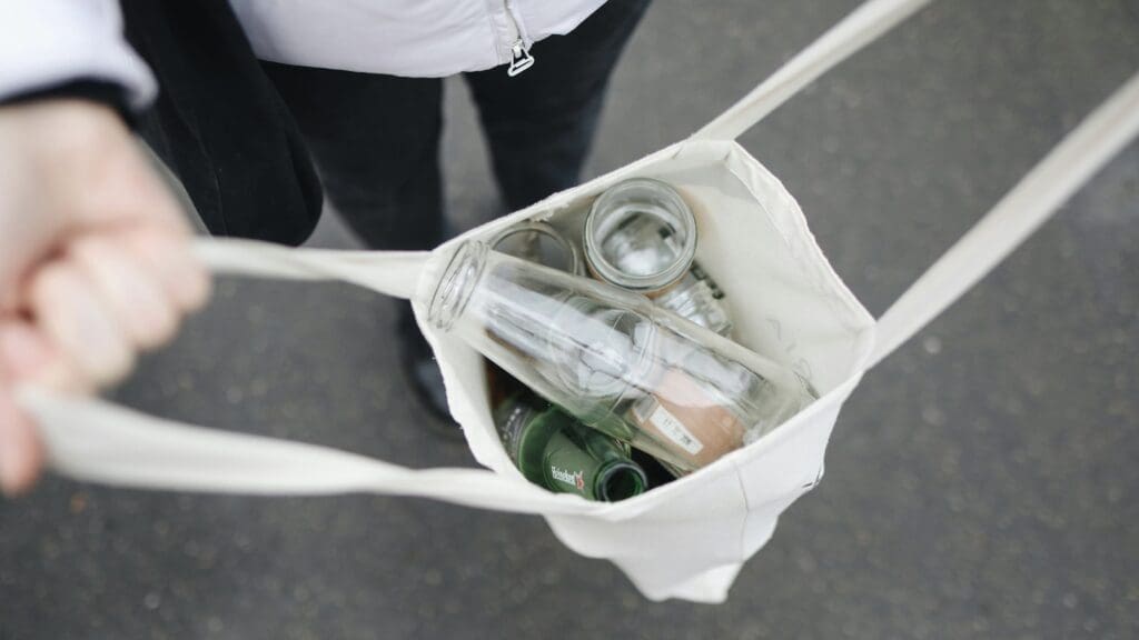 Person holds open reusable bag full of recyclable items such as bottles and cans.
