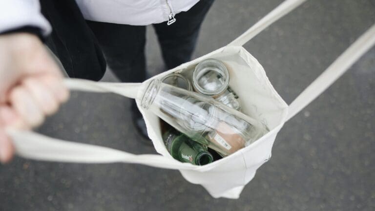 Person holds open reusable bag full of recyclable items such as bottles and cans.