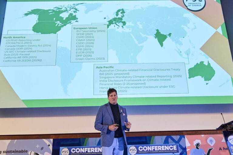 James George stands on stage in front of a screen that has a map of the world on it with list of legislations.