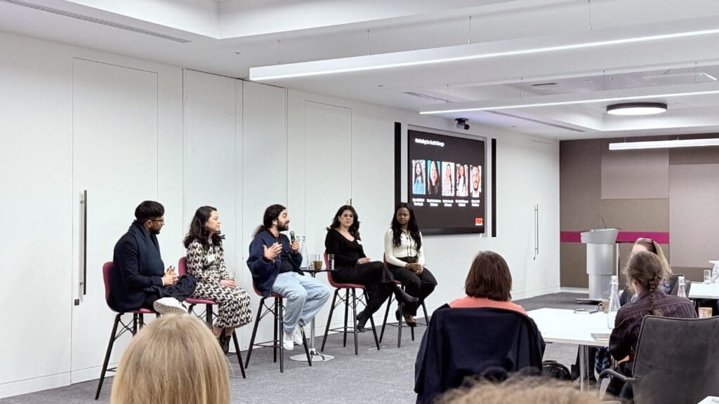Five people sit on chairs at the front of a room, facing an audience