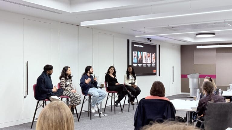 Five people sit on chairs at the front of a room, facing an audience